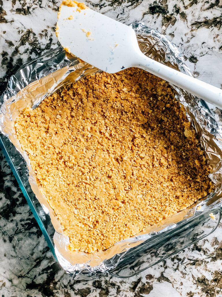 The crushed golden Oreos and melted butter mixture pressed in the foil lined dish to make the crust of this no bake dessert.