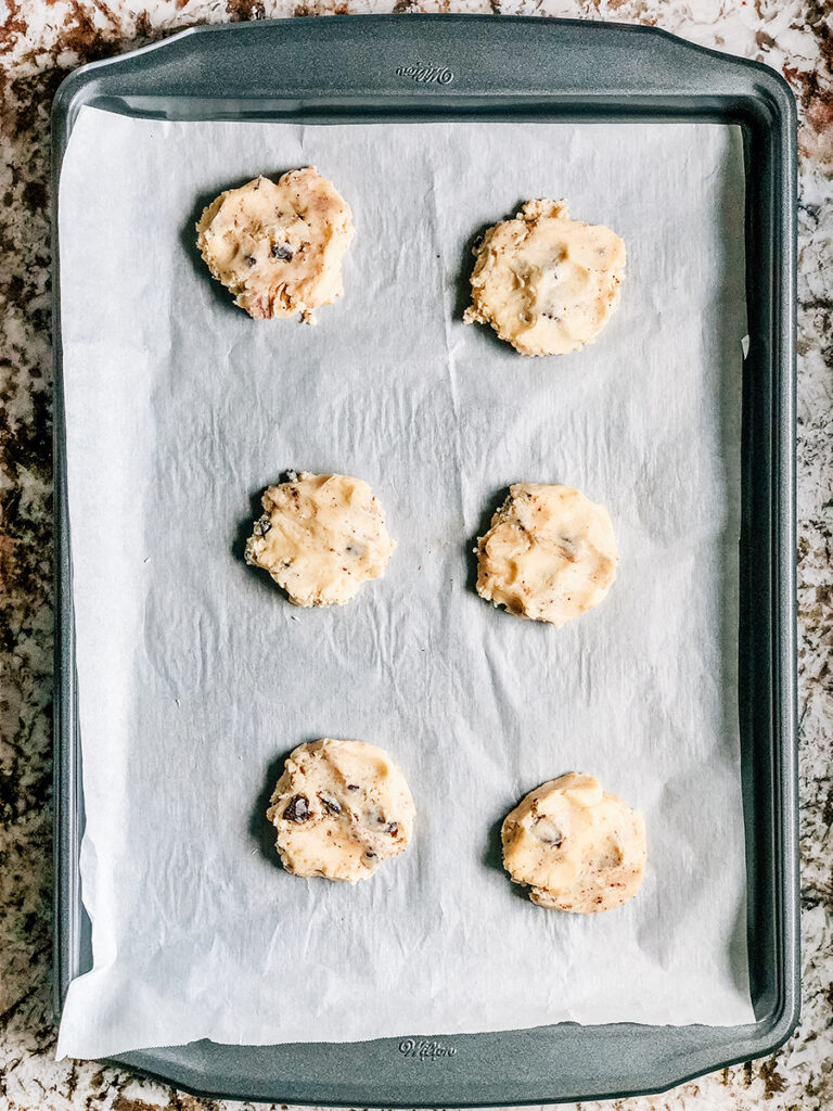 Two tablespoon dough balls slightly flattened on a parchment lined cookie sheet.