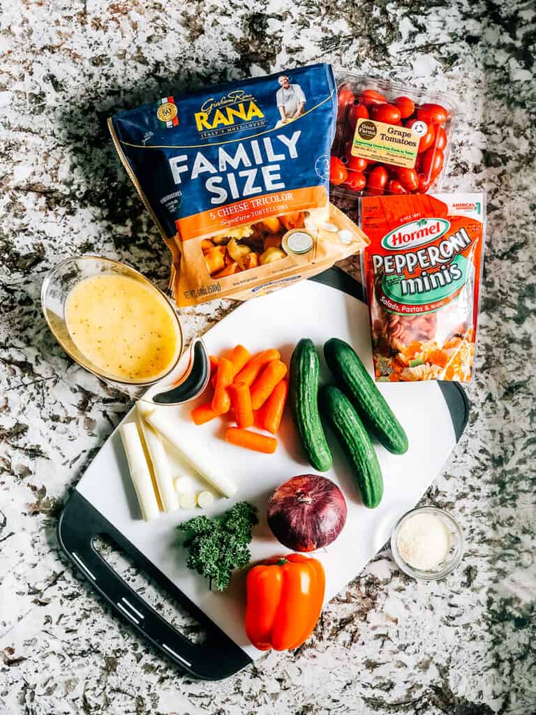 The ingredients for Italian Tortellini Salad: 5 cheese tricolor tortellini, grape tomatoes, mini pepperoni, cucumbers, carrots, orange bell pepper, mozzarella cheese, Italian dressing, grated parmesan cheese, and fresh parsley.