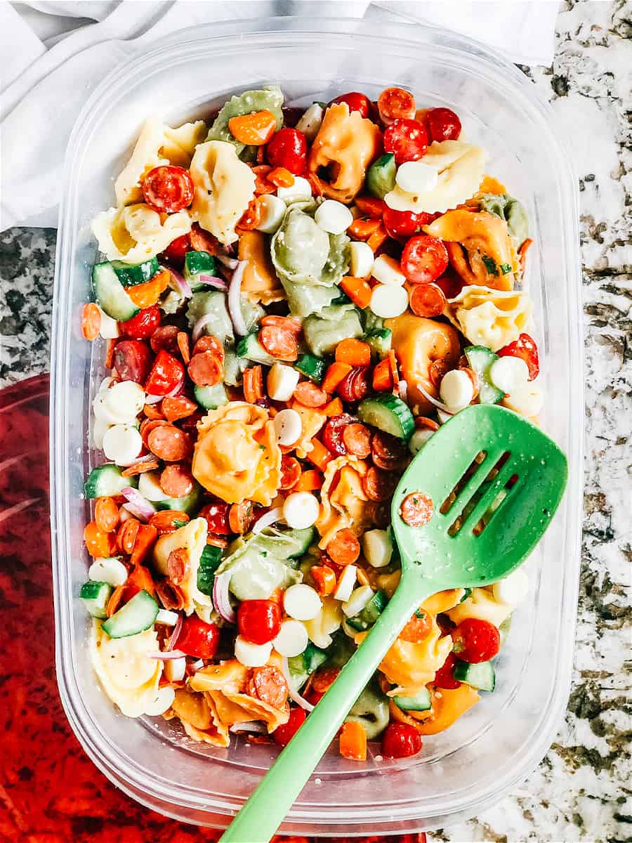 Photo of Italian Tortellini Salad in a clear Tupperware container with a green spoon - by The Recipe Life
