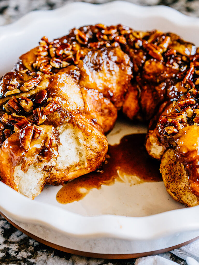Monkey bread a pie plate showing the fluffy bread covered in chopped pecans and a sweet glaze.