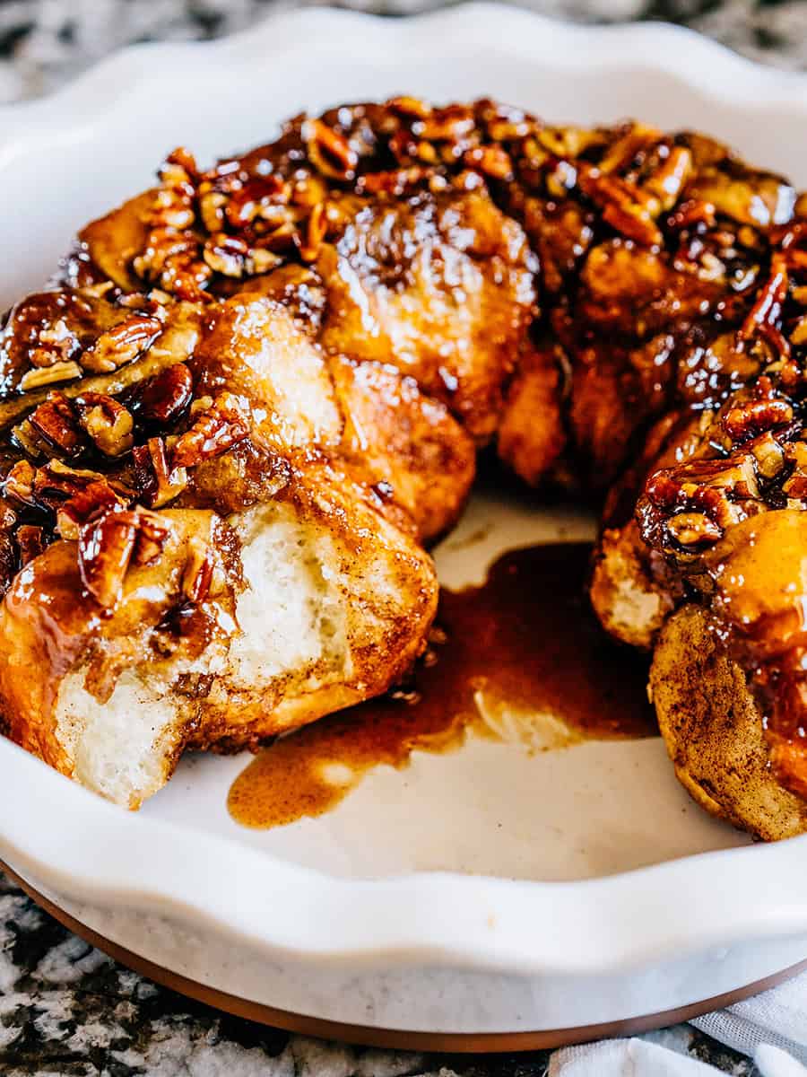 Monkey bread dans un moule à tarte montrant le pain moelleux recouvert de noix de pécan hachées et d'un glaçage sucré.