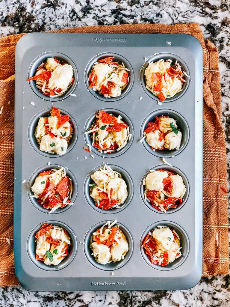 The pizza muffin mix with tons of mozzarella cheese and pepperoni in the muffin tins.