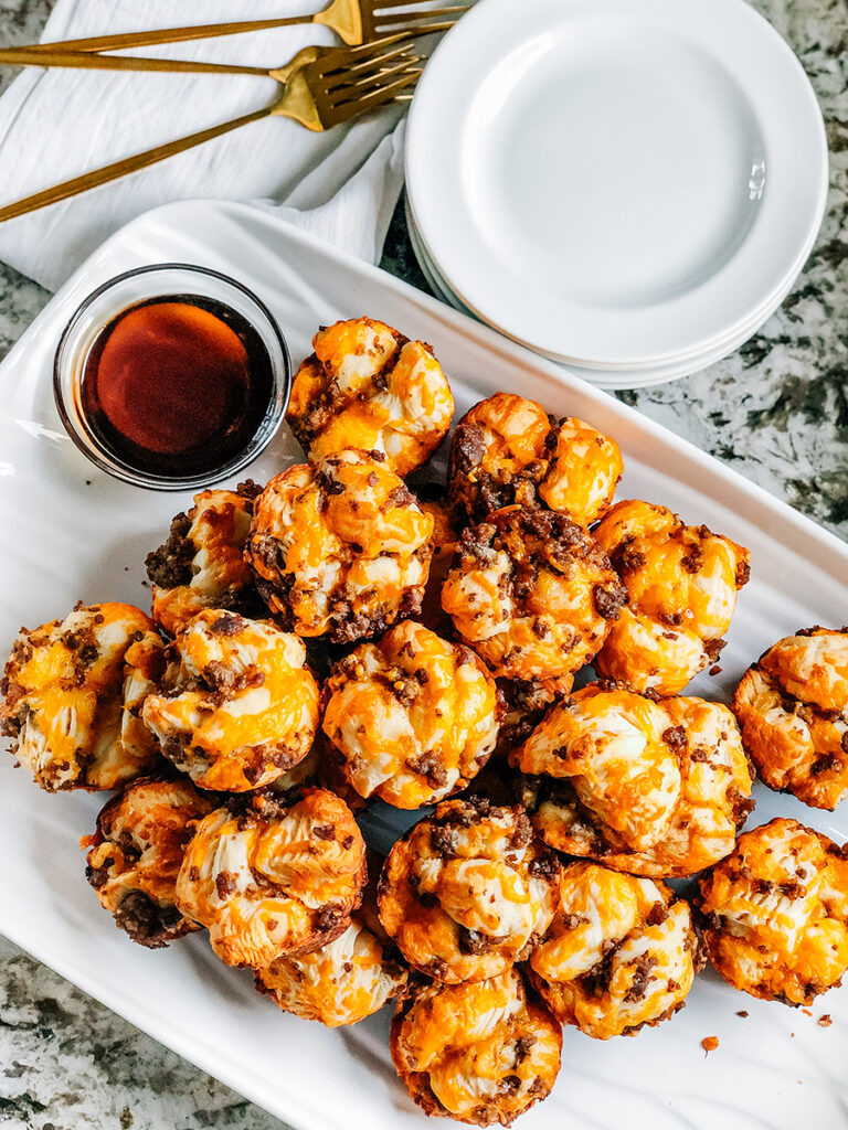 Sausage Breakfast Muffins piled high on a serving plate with pancake dipping sauce on the side. They are the perfect hands on breakfast idea.