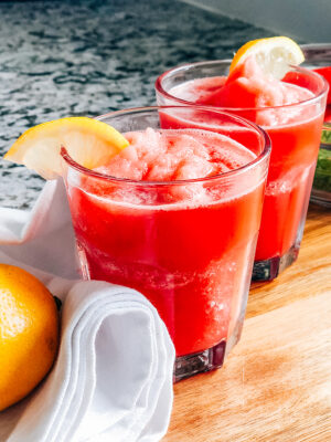 Two glasses of frozen watermelon lemonade garnished with lemon slices.