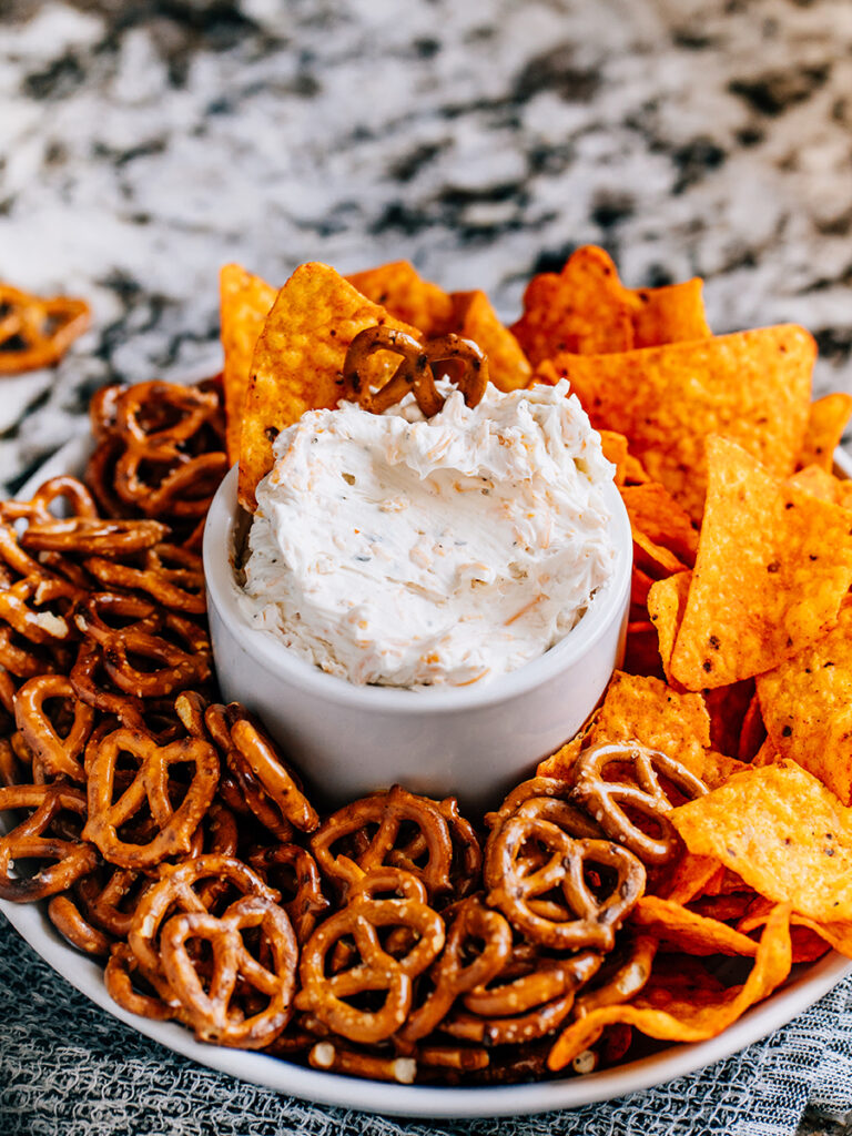 This cold beer dip is surrounded by doritos and pretzels.