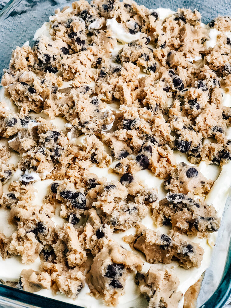 Crumbled cookie dough on top of a layer of cheesecake batter and more chocolate chip cookie dough.