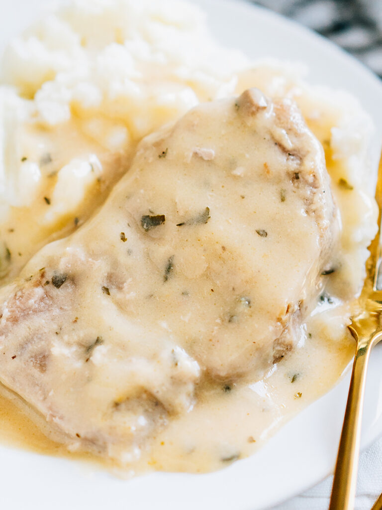 A juicy and tender pork chop laying on mashed potatoes and covered in a creamy gravy.