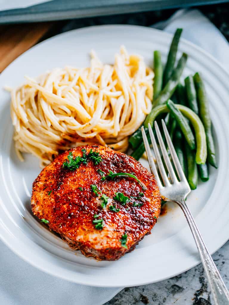 A flavorful easy baked pork chop made with brown sugar and spices plated with a side of garden beans and spaghetti alfredo.