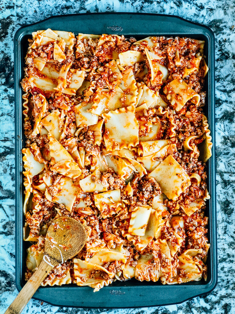 The lasagna noodles and meat sauce mixture evenly poured onto a sheet pan.