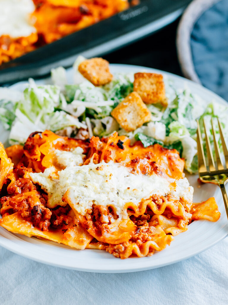 A plated serving of this traditional lasagna made in a sheet pan with a side of Caesar salad.
