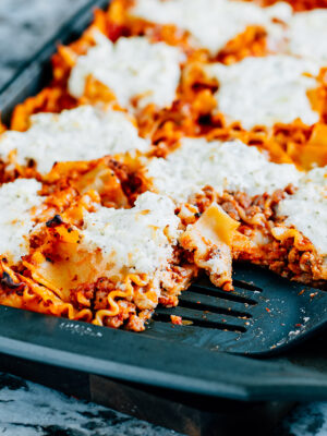 A delicious pan of sheet pan lasagna with a serving spatula in it.