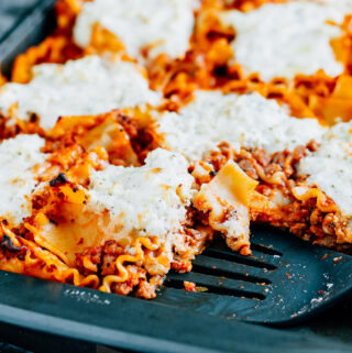 A delicious pan of sheet pan lasagna with a serving spatula in it.
