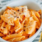 A serving dish piled high of penne pasta with a cottage cheese and marinara pasta sauce garnished with shredded parmesan cheese and red pepper flakes.