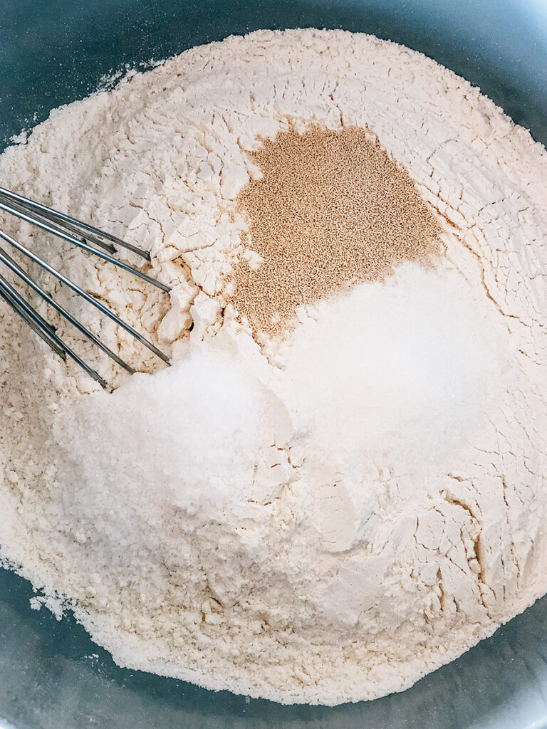 Flour, sugar, salt, and yeast in a large bowl ready to be whisked together.