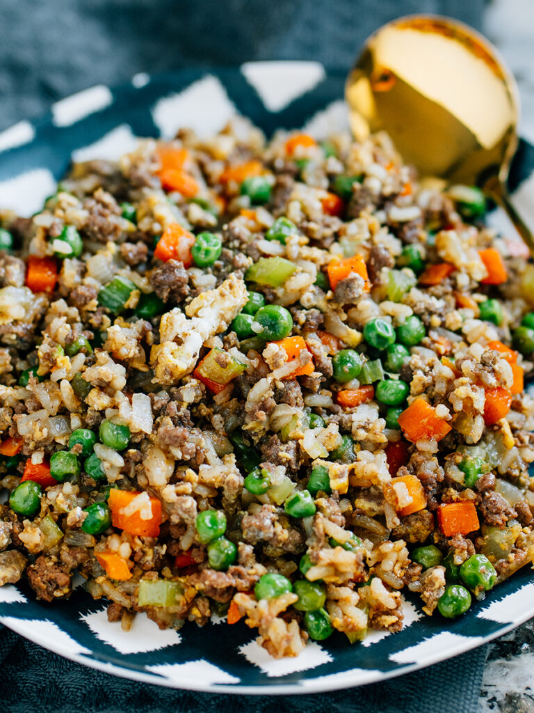 A deep black and white plate filled with ground beef, cooked rice and scrambled egg covered in a soy sauce or aminos which is this amazing beef fried rice recipe.