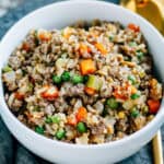 A bowl filled with beef fried rice which is tender peas, carrots and celery cooked with browned ground beef, scrambled eggs and cooked rice.