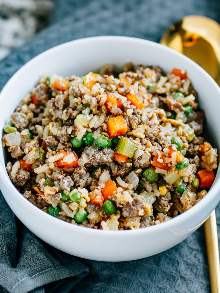 A bowl filled with beef fried rice which is tender peas, carrots and celery cooked with browned ground beef, scrambled eggs and cooked rice.