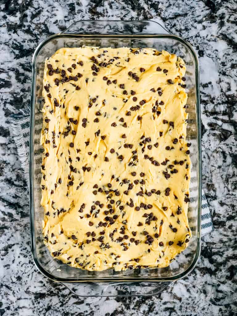 The lazy chocolate chip cookie bar dough spread in a 9x13 in glass baking dish.