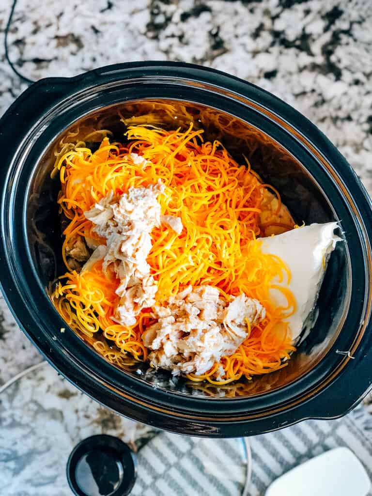 All ingredients of buffalo chicken dip in the slow cooker.