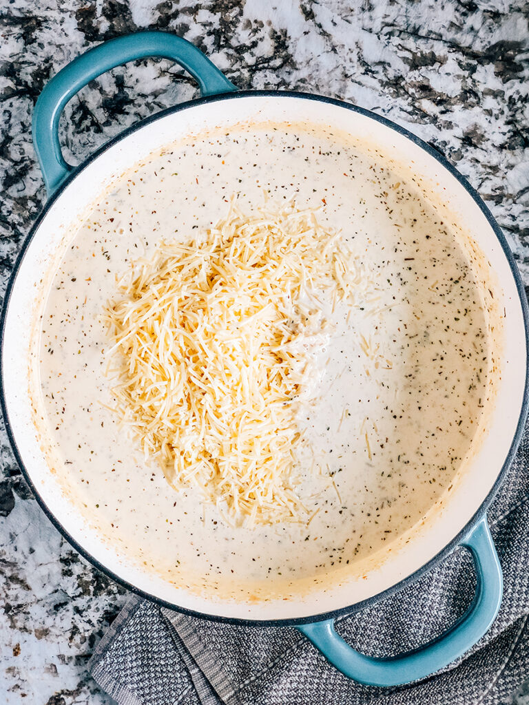 Adding shredded parmesan cheese to the seasoned white sauce to make a creamy homemade alfredo.