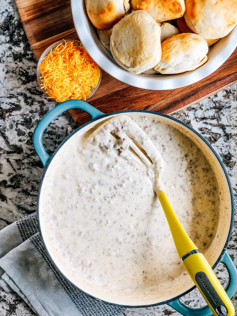 A large skillet of sausage gravy with freshly baked biscuits ready to be served.