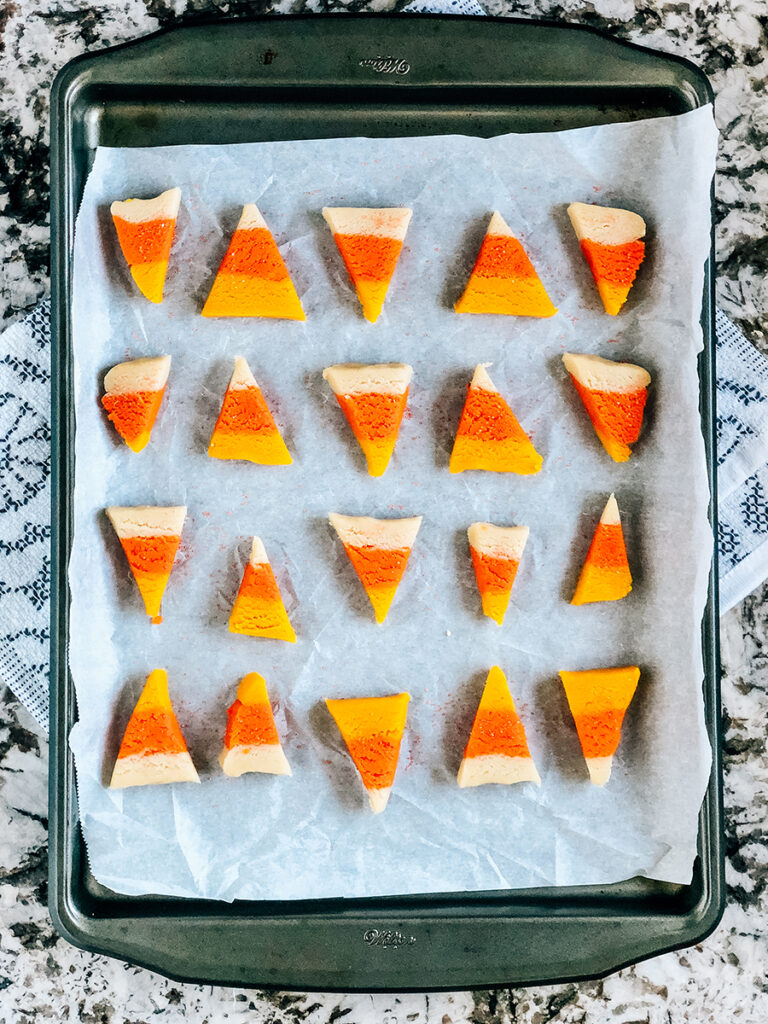 A pan of candy corn shaped sugar cookies on a baking sheet lined with parchment paper.