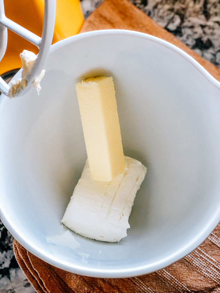 A Stick of butter and block of cream cheese in a stand mixer bowl.