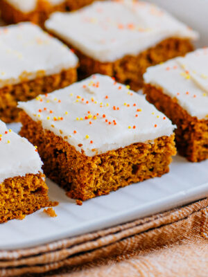 A pumpkin bar frosted with cream cheese icing on a serving plater.