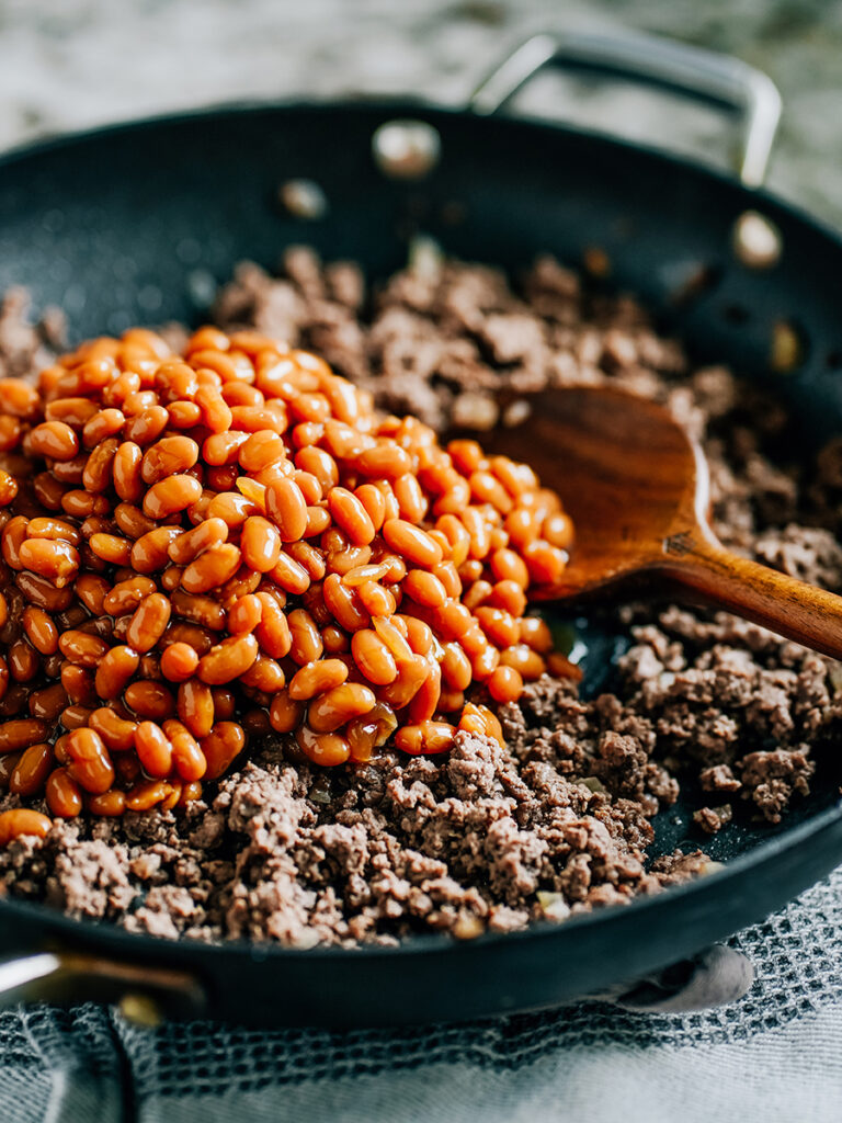 A skillet with brown ground beef and a pile of baked beans on top of it.