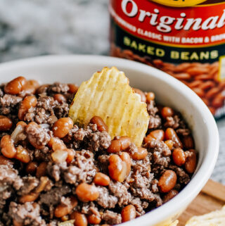 Beef and beans in a bowl with a chip dipped into them.