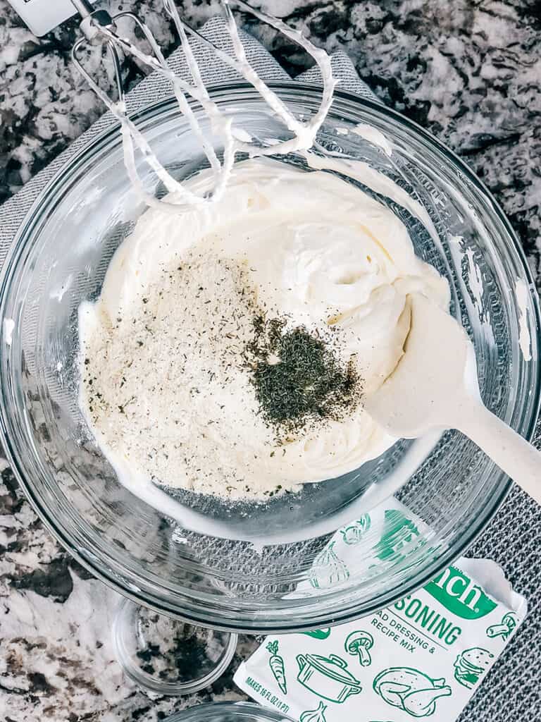 Ranch seasoning packet and dill on top of sour cream and cream cheese.