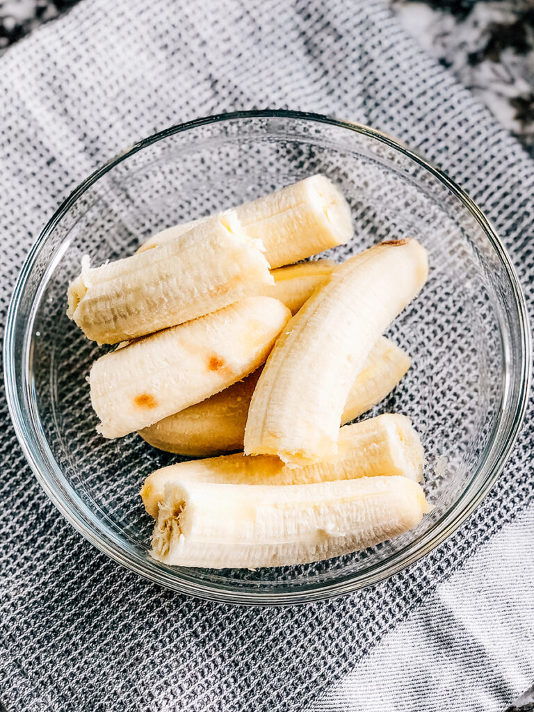 Four ripe bananas peeled in a glass bowl.