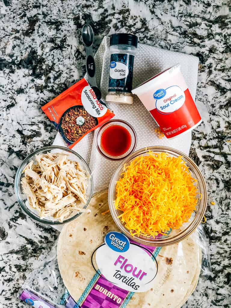 ingredients for easy chicken quesadillas: Cooked shredded chicken, shredded cheddar cheese, sour cream, taco seasoning, garlic salt, hot sauce, and tortillas!