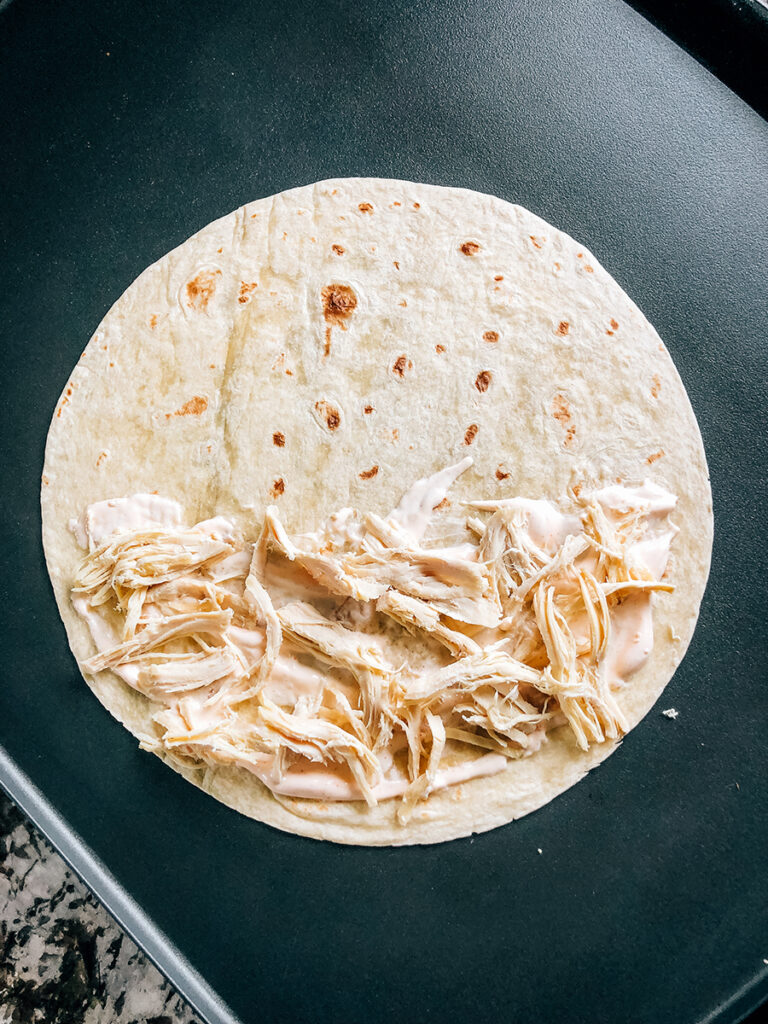 A layer of cooked shredded chicken added on top of sauce to the tortilla.