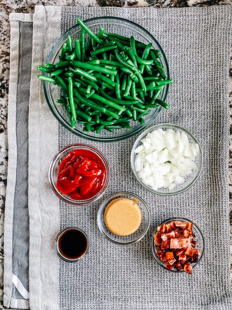 The six ingredients for BBQ green beans: drained green beans, ketchup, brown sugar, Worcestershire sauce, cooked bacon and onions.