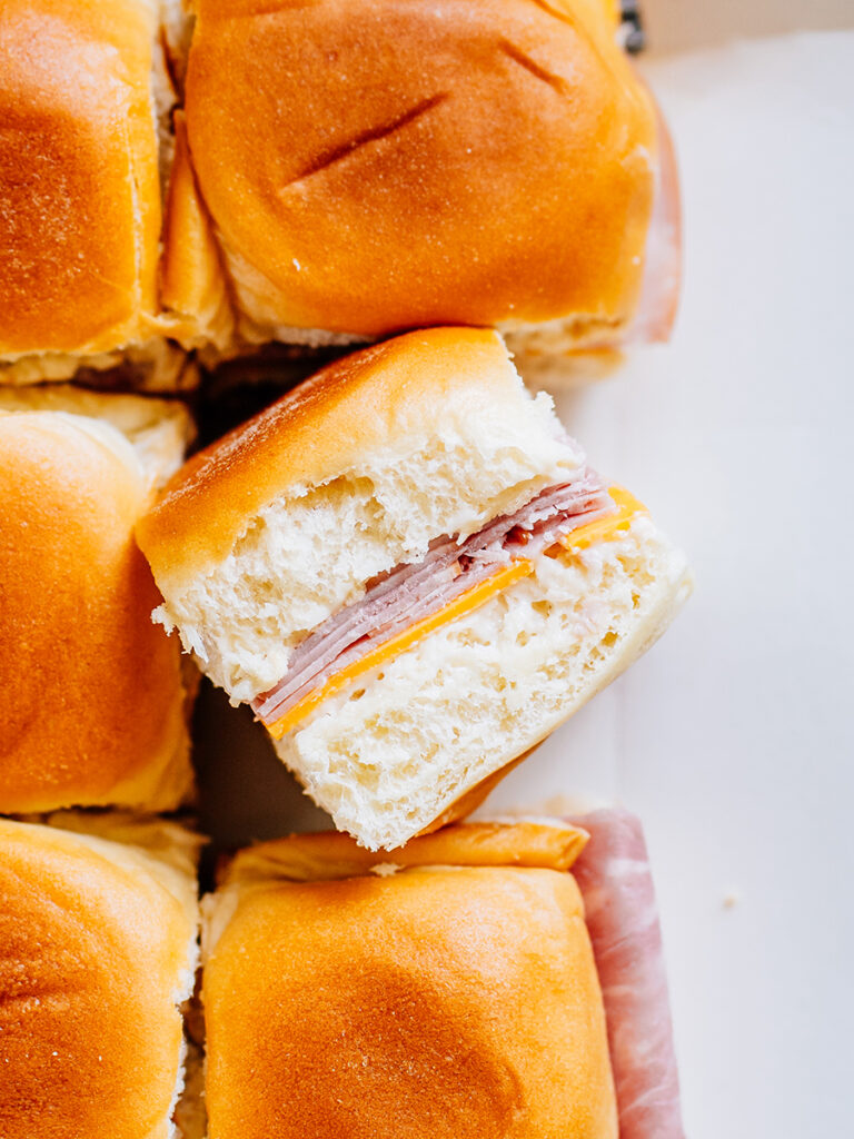 A ham and cheese slider on its side to show the inside layer of Miracle Whip, sliced cheese, and deli ham.