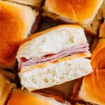 A savory cold ham and cheese slider on it's it side surrounded by other sliders sitting upright.