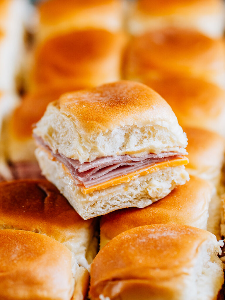 Close up of one Ham and Cheese slider in top of a bunch of other sliders.