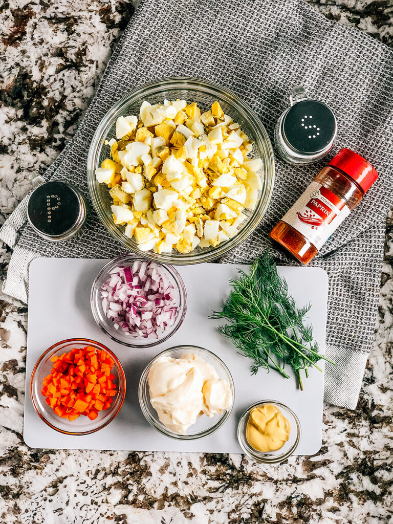 The ingredients for the best egg salad: Chopped hard-boiled eggs, diced carrot, diced red onion, Miracle Whip, dijon mustard, paprika, salt, and pepper.