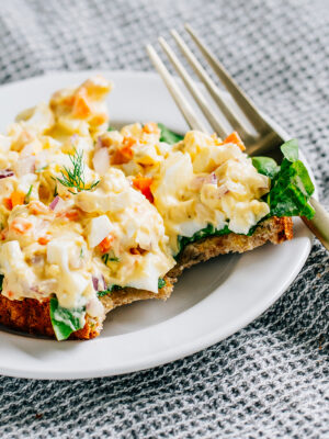 Egg salad on buttered wheat toast and garden lettuce with bites taken out.