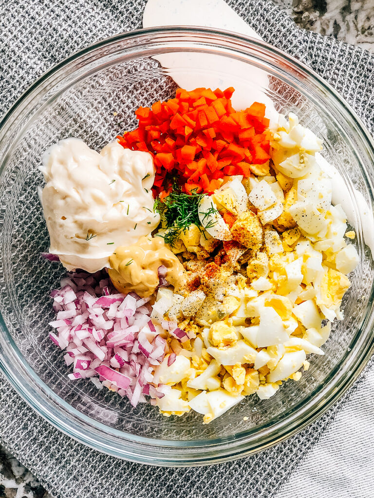 All ingredients to egg salad in a glass bowl ready to be mixed into a tasty breakfast, lunch, or snack.