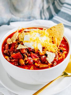 Taco soup in a bowl garnish with sour cream, cheddar cheese, and crushed tortilla chips.