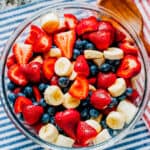 Another view of honey lime coated fresh strawberries, blueberries, and bananas in a large glass bowl.