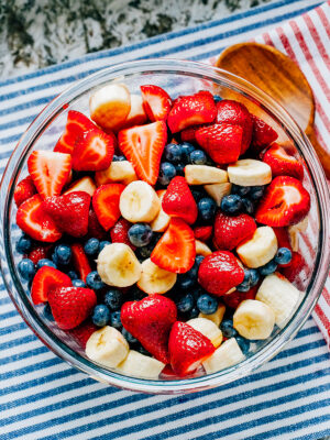 Another view of honey lime coated fresh strawberries, blueberries, and bananas in a large glass bowl.