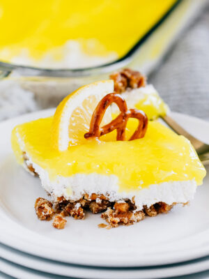 Tart lemon pie filling spread on a sweet and creamy cream cheese and Cool Whip layer and buttery pretzel crumb crust is this lemon pretzel dessert plated and ready to be enjoyed!