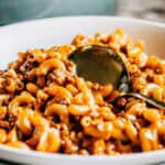 White bowl of homemade hamburger helper noodles and ground beef coated in a cheese sauce.