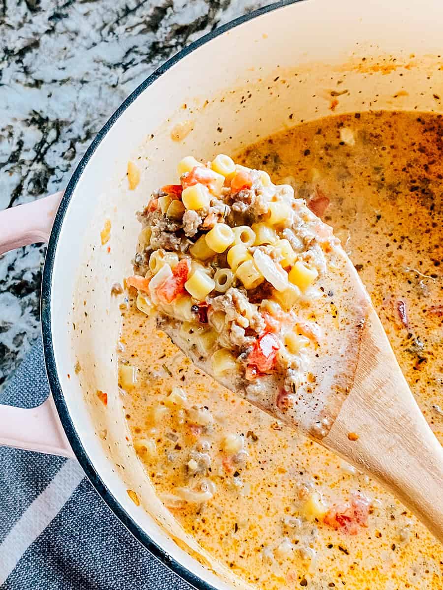 Une louche en bois pleine de soupe crémeuse à la saucisse italienne avec de petites pâtes ditalini et des tomates en dés.