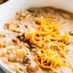 Creamy Hamburger Potato Soup with a sprinkle of shredded cheddar cheese in a white bowl.