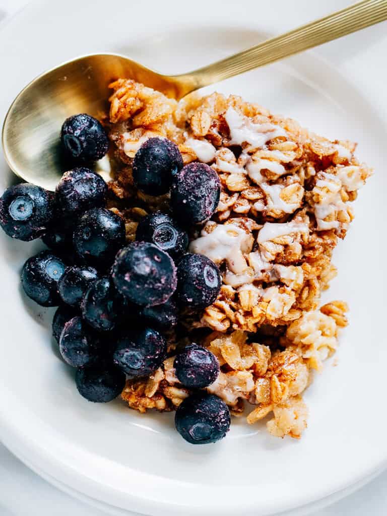 Overview: Softened hearty oats covered in sweet cinnamon sugar drizzled with a simple glaze and topped with frozen blueberries plated and ready to eat.